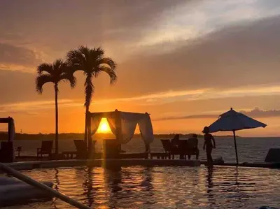 a person standing next to a swimming pool with a sunset at Velero Beach Cabarete 2 bedroom Penthouse in Cabarete