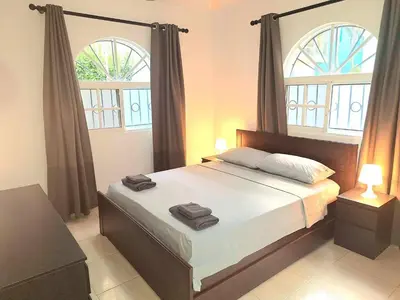 a bedroom with a large bed with two windows at Apartamento Oasis PUNTA CANA in Punta Cana