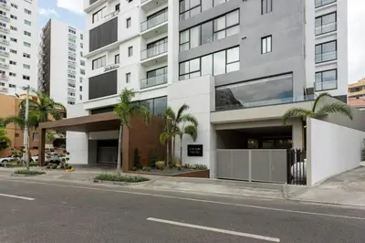 a large building on a city street with palm trees at Encantador Apto en Torre de Lujo, Piscina, AC & Parking in Santo Domingo