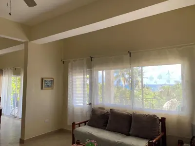 a living room with a couch and a large window at 2BR & 2 WR ocean view Suite at Villa Costa Verde in Playa Cofresi, Puerto Plata, with a pool, big veranda, and a rooftop terrace in San Felipe de Puerto Plata