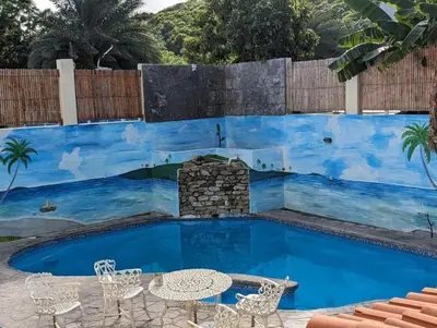 a pool with tables and chairs in front of a painted wall at 2BR & 2 WR ocean view Suite at Villa Costa Verde in Playa Cofresi, Puerto Plata, with a pool, big veranda, and a rooftop terrace in San Felipe de Puerto Plata