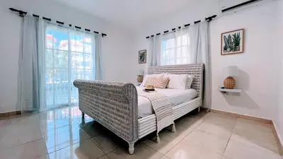 a bedroom with a bed and a wicker chair at Pool View, Walk to Beach, Shops, Dining, Fast Wifi in Punta Cana