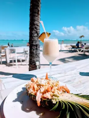 a plate of food with a drink on the beach at Rooftop, Pool View, Walk to Beach, Dining, Shops in Punta Cana