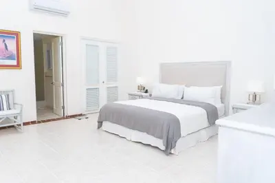 a white bedroom with a large bed and a bathroom at Cacique 13, Ocean View and Golf Course in La Romana