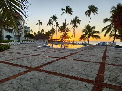 an empty beach with palm trees and a sunset at Confortable vista al mar in Juan Dolio