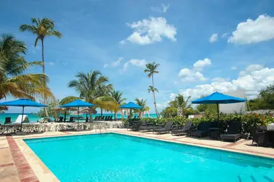 a swimming pool with chairs and blue umbrellas at 2BR 2BA Beachfront With View 62 in Bayahibe
