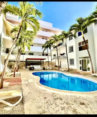 a swimming pool in front of a building with palm trees at Central in Punta Cana Beach Life RD in Punta Cana