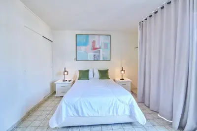 a white bedroom with a white bed and two night stands at A Beautiful Studio Apartments Furnished in Gascue in Santo Domingo
