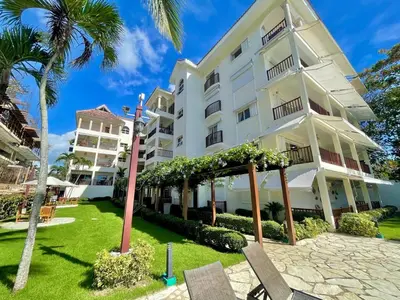 a large white building with chairs and palm trees at Spacious apartment beach access in Juan Dolio