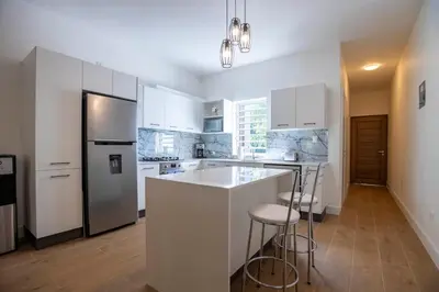 a kitchen with white cabinets and a large island with bar stools at Perla Marina Beachside Apartment in Bombita