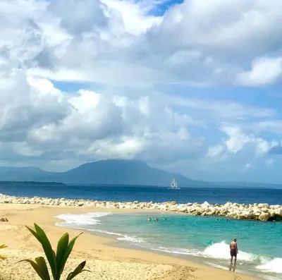 a person walking on a beach with a sail boat in the water at Infiniti blu beautiful apartment at the pool in Sosúa