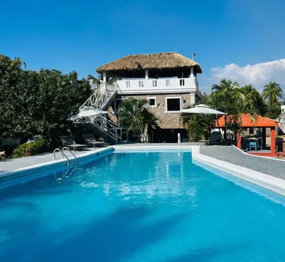 a swimming pool in front of a house with a thatch roof at Villa Rosa Bella Perfect for families or groups in Palmar de Ocoa