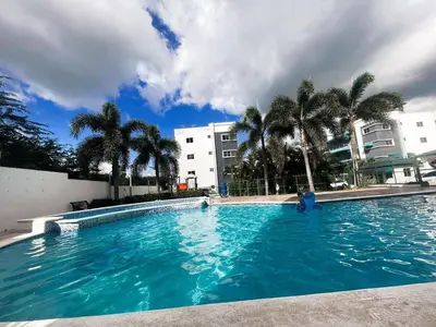 a large blue swimming pool with palm trees and buildings at Apartment in Harmony I in Santiago de los Caballeros