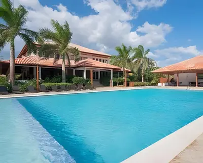 a pool in front of a house with palm trees at Club Hemingway Amplio Apartamento en la Playa de Juan Dolio in Los Corrales