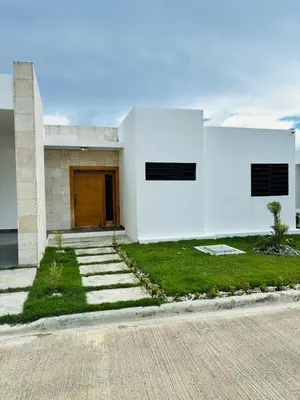 a white building with a brown door and grass at El Rincon Soleado in San Felipe de Puerto Plata