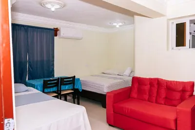 a room with two beds and a red chair at Apartahotel Santo Domingo EsteRD - Aeropuerto Las Americas in La Viva