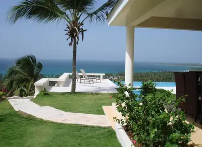 a patio with a table and a palm tree and the ocean at Villa with Stunning Ocean View, Infinity pool in Las Terrenas