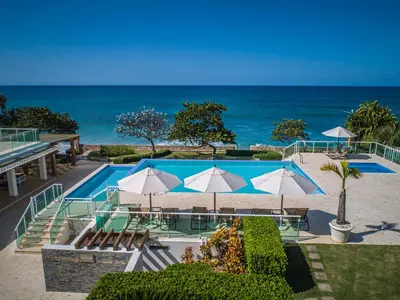 a pool with tables and umbrellas and the ocean at Tropical Gem by the Sea in Sosúa
