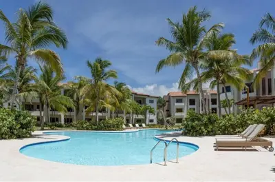 a swimming pool with palm trees and condos at Suite tropical in Punta Cana