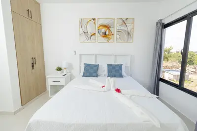 a white bedroom with a large white bed with a window at Cozy 2BR Apartment in Sunshine Bayahibe in San Rafael del Yuma