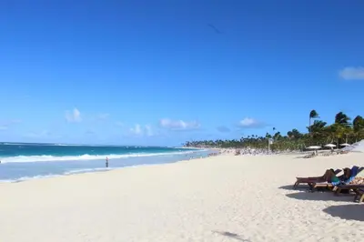 two people are sitting on benches on a beach at Blue Paradise Punta Cana in Punta Cana