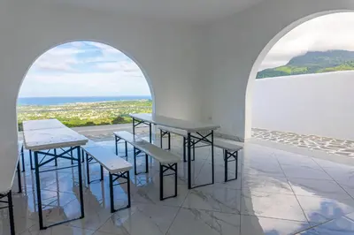 a room with two tables and benches and a view of the ocean at Grecialandia in San Felipe de Puerto Plata