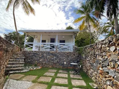 a house with a stone wall and palm trees at The Cottage at Javo beach in Las Galeras