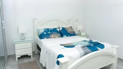 a white bed with blue pillows in a white bedroom at Villa Rosa Boca Chica in Boca Chica