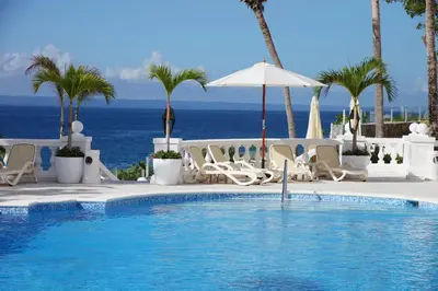 a swimming pool with chairs and an umbrella and the ocean at Bahia Principe Grand Samana - Adults Only in Santa Bárbara de Samaná