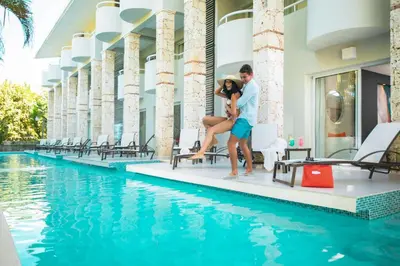 a couple sitting next to a swimming pool at a hotel at Emotions by Hodelpa - Juan Dolio in Juan Dolio