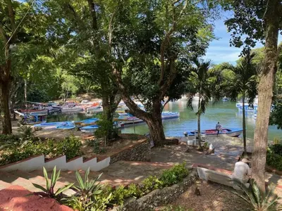 a woman sitting on a bench next to a river with boats at Room 3 in Río San Juan