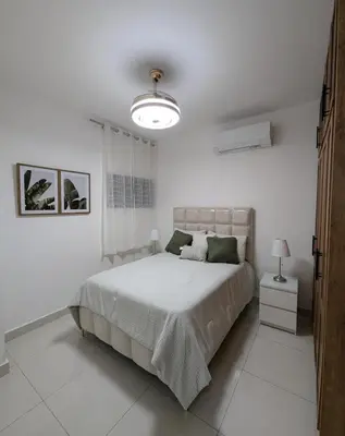 a white bedroom with a large bed and a lamp at Escapada perfecta, apartamento frente al mar in San Felipe de Puerto Plata