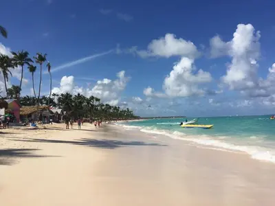 a beach with people and a boat in the ocean at Spacious 2 Bedroom Condo with Pool close to Beach in Punta Cana