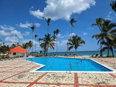 a pool on the beach with palm trees and the ocean at Sea front apartment, Juan Dolio, San Pedro in San Pedro de Macorís