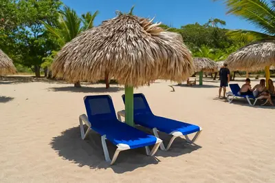 two blue chairs under a straw umbrella on the beach at CortLang Vacation Rentals, Costambar in San Felipe de Puerto Plata