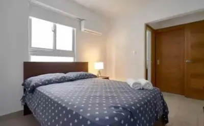 a bedroom with a bed with a blue comforter and a window at Encanto en gazcue - Cerca del Malecón y la Zona Colonial in Santo Domingo
