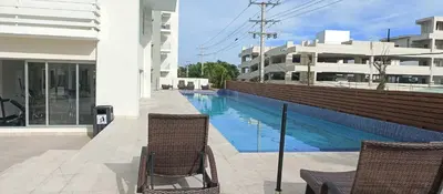 a swimming pool next to a building with two chairs at Apartamento en Boca Chica T3 602 in Boca Chica