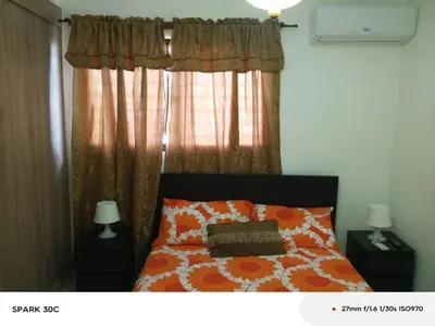 a bed with an orange and white comforter and a window at Hermoso Apartamento de tres habitaciones in La Viva