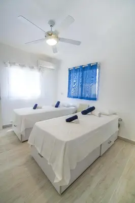 two beds in a white room with a ceiling fan at Le Camere Del Maestro in Bayahibe