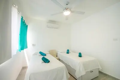 two beds in a white room with blue pillows at Le Camere Del Maestro in Bayahibe