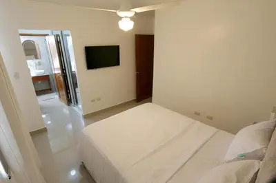 a white bedroom with a bed and a flat screen tv at Lujoso Pent-house en el Residencial Mediterráneo in Santiago de los Caballeros