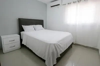 a white bedroom with a bed and a window at Lujoso Pent-house en el Residencial Mediterráneo in Santiago de los Caballeros