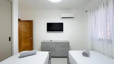 a white room with two beds and a television at Luxury Apartment-PRIVATE Patio & BBQ-Near Airport in Santiago de los Caballeros