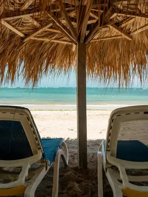 two chairs under a straw umbrella on the beach at Ocean Winds Hotel in San Felipe de Puerto Plata