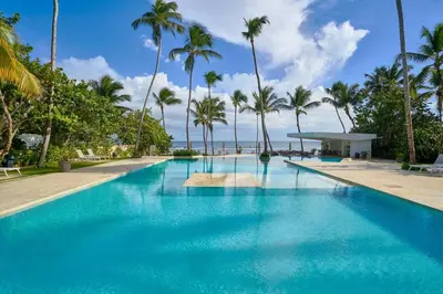 a swimming pool with palm trees and the ocean at Caribbean Paradise Aquarella 22th in La Puntica de Juan Dolio