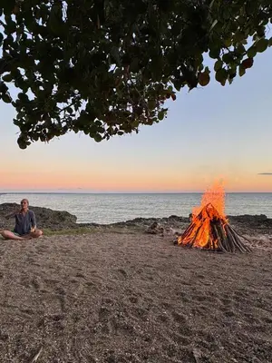 a man sitting next to a bonfire on a beach at Ki-Ra Holistic Living in Boca de Chavón