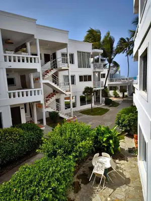 a white apartment building with two chairs and palm trees at Chilvers Seaside Studio 202 in Cabarete