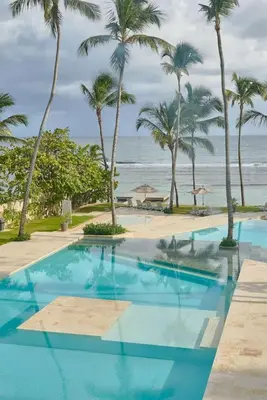 a swimming pool with palm trees and the ocean at Beachfront FL21 Con Tina Aquarella in La Puntica de Juan Dolio