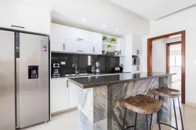 a kitchen with white cabinets and a counter with stools at 2BR Tropical Escape - Private Terrace, BBQ, Pool, Walk to Beach in Punta Cana