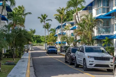 a street with cars parked on the side of a road with palm trees at Resort Villas | 2 hab con piscina y playa in Juan Dolio